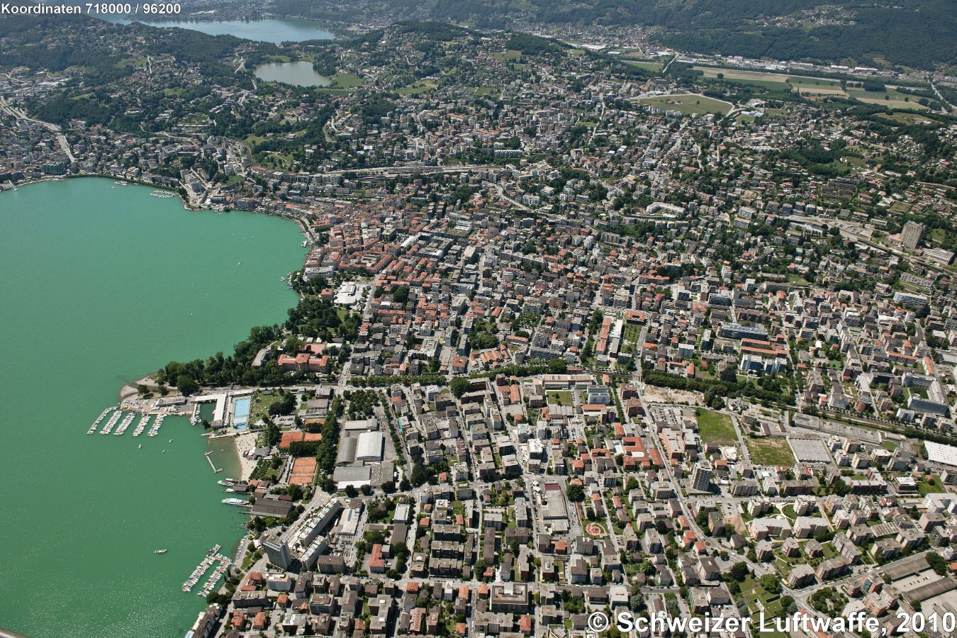 Lugano, Blickrichtung SW. Obere linke Bildecke: Caslano, vorgelagert Lago di Muzzano (Position 2'715'430.46, 1'095'010.47), westlich davon am Bildrand: Agno am Lago di Lugano. Oberer Bildrand Mitte: Breganzona, NW davon: Bioggio. Oberer Bildteil rechts: Massagno. Dem Lido (Delta des Cassarate) nordwärts vorgelagert: Centro Esposizioni Padiglione Conza (Position: 2'718'162.56, 1'096'181.04). Università della Svizzera Italiana (USI; Position 2'717'678.84, 1'096'649.68) ca. untere Bildmitte westlich des Flusses Cassarate.